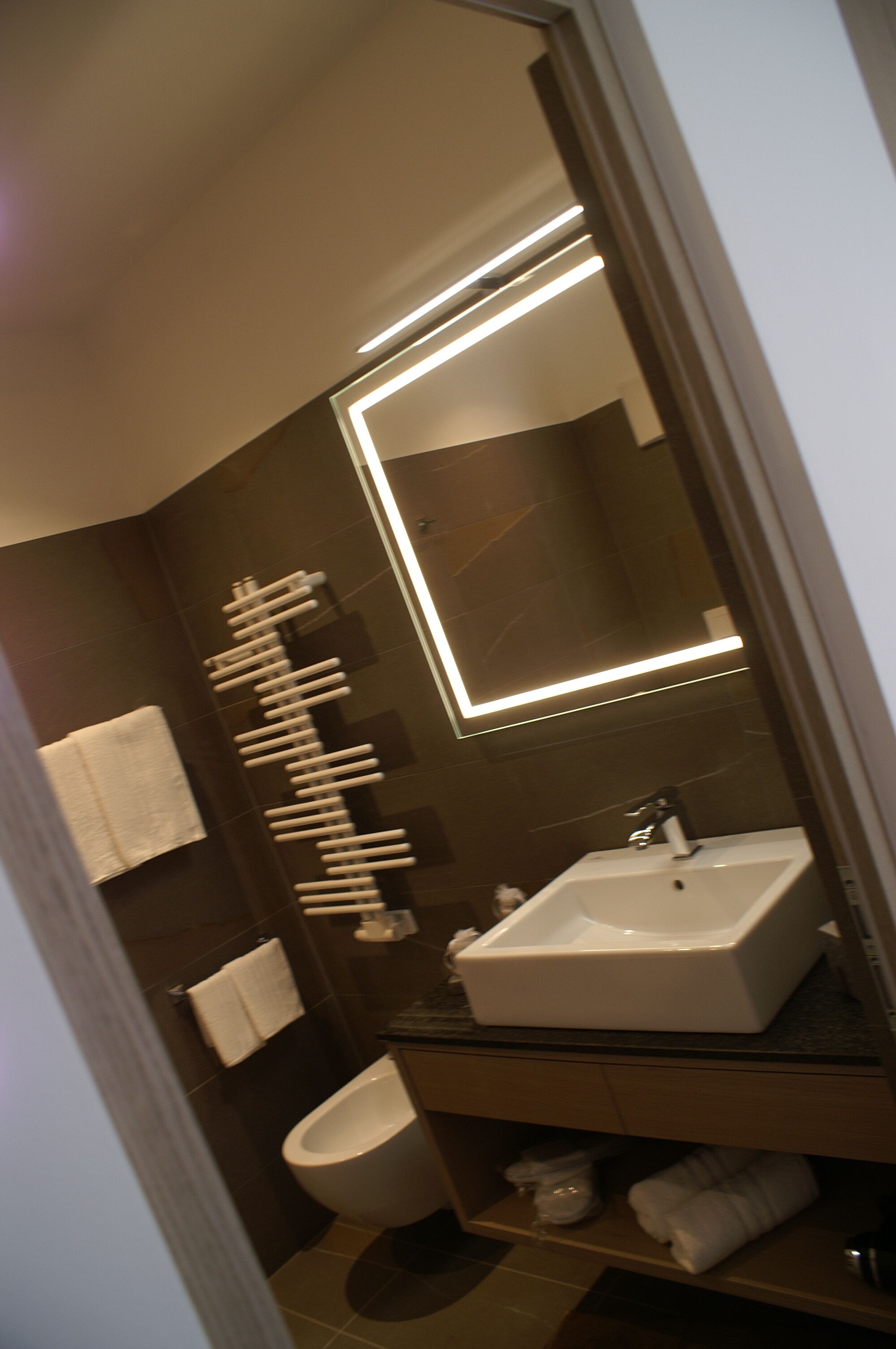Un bagno moderno con un lavandino bianco, uno specchio e un porta asciugamani.