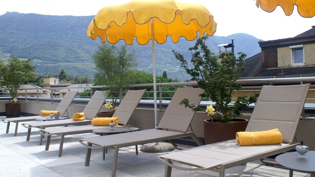 A rooftop terrace with lounge chairs, yellow umbrellas, and potted plants. - Residence Villa Hedy (Merano)
