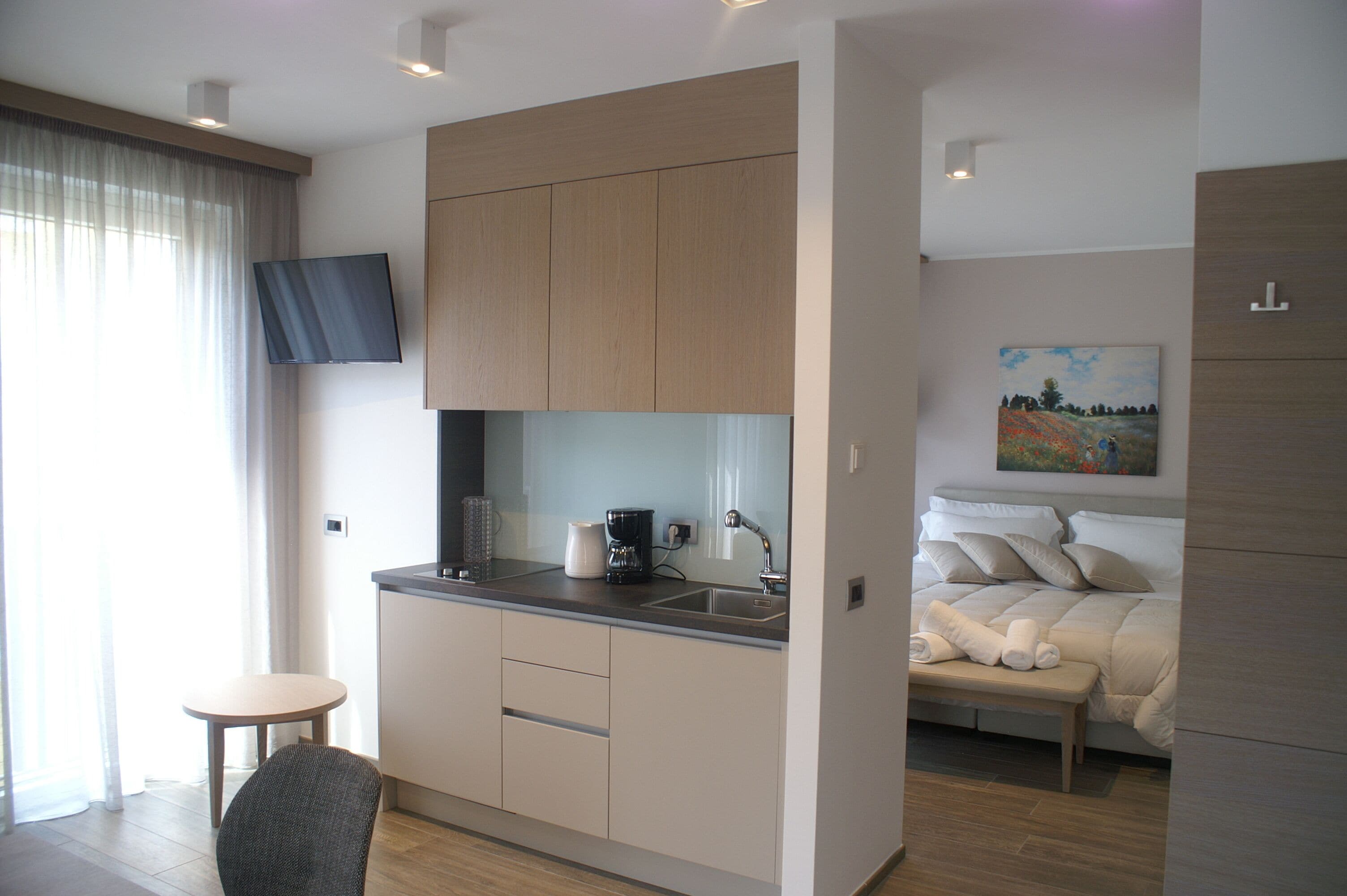 Una habitación de hotel moderna con kitchenette, una cama, un cuadro y un televisor.