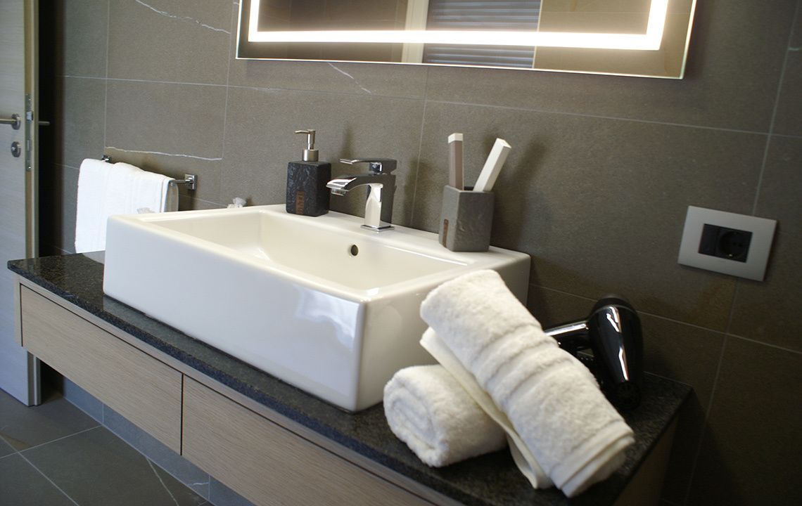 A modern bathroom with a large sink, towel rack, and a mirror with built-in lighting.