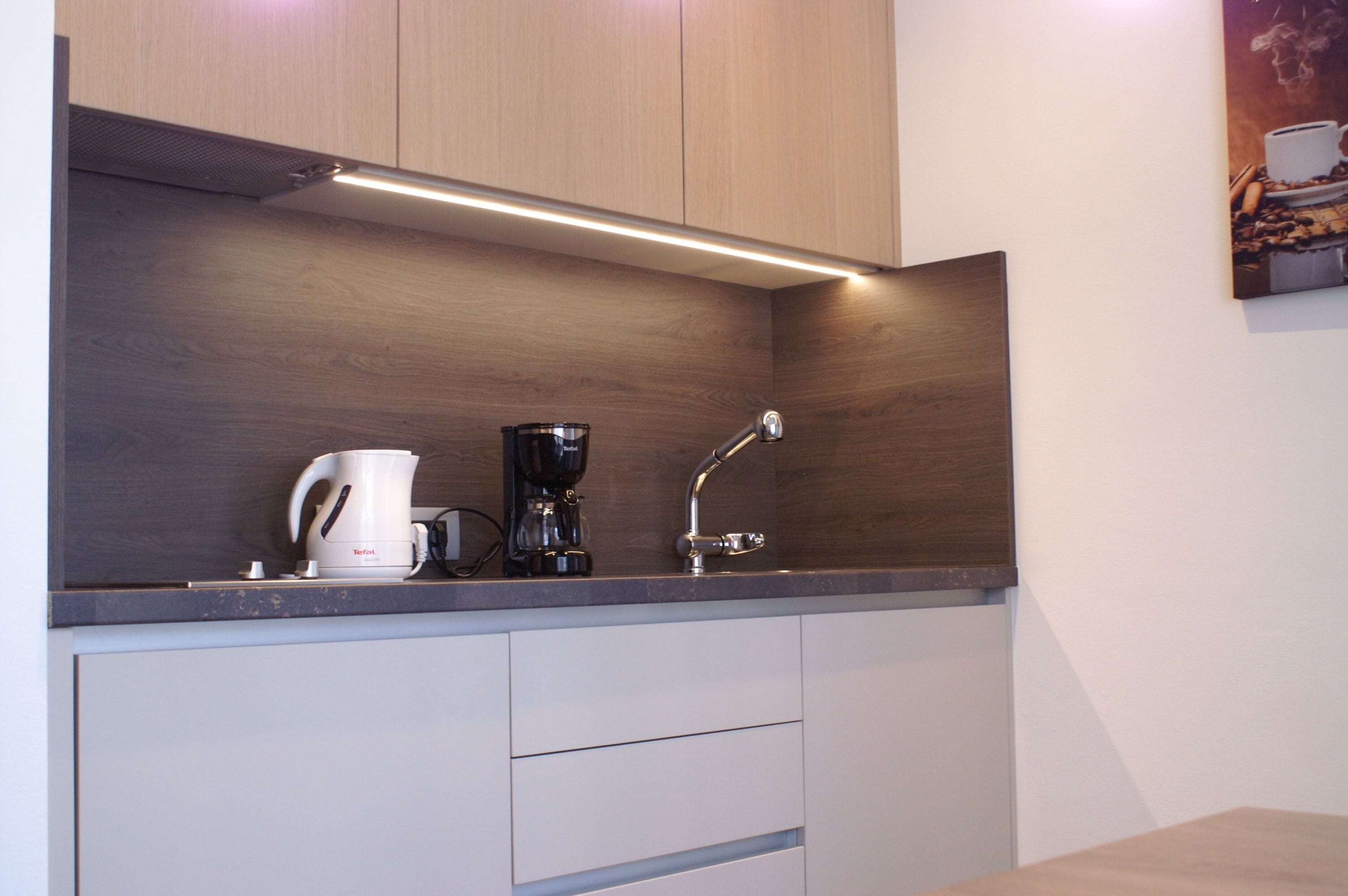 A modern kitchen with wooden cabinets, a built-in coffee maker, and a sleek countertop.