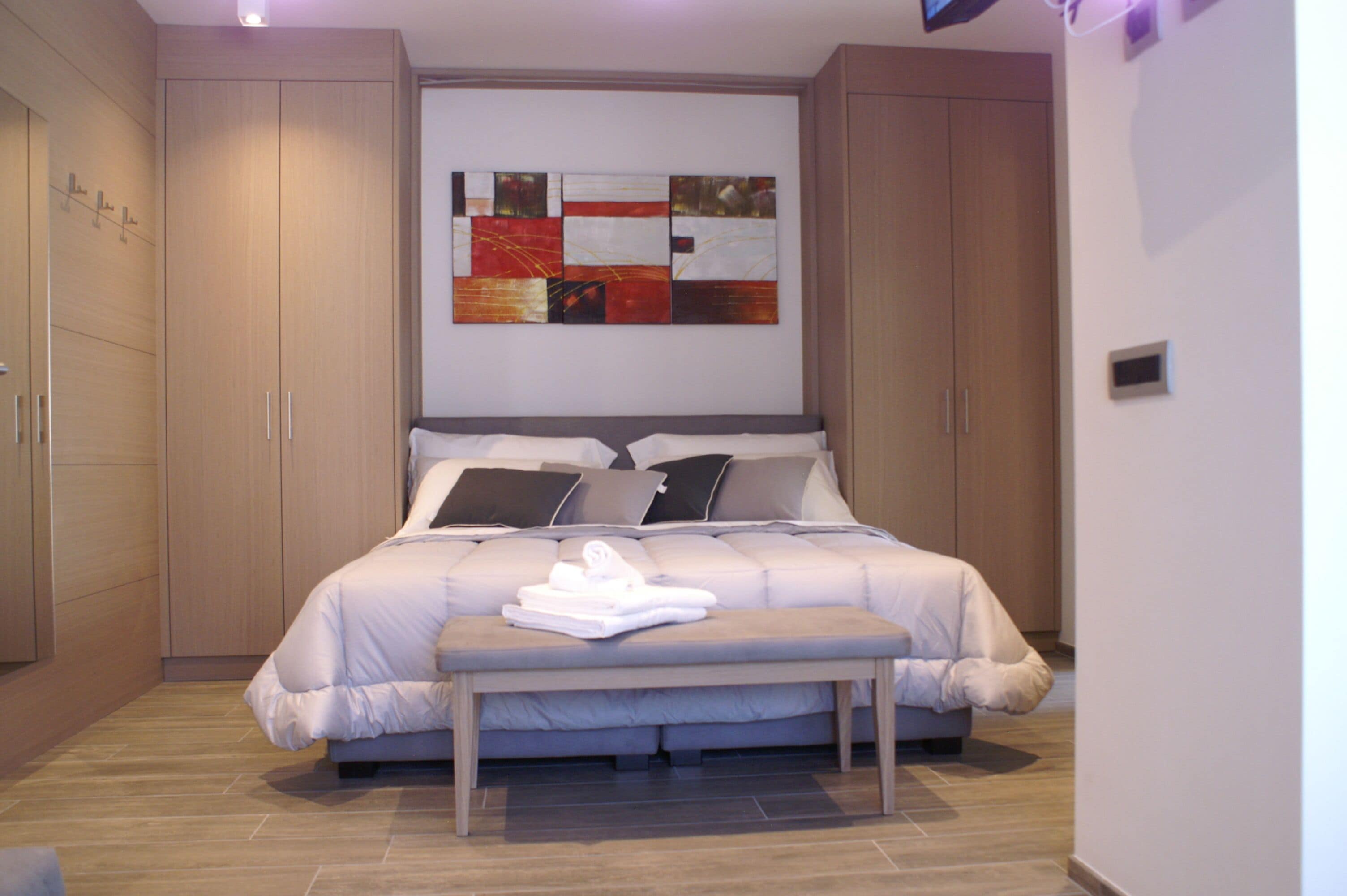 A bedroom with a large bed, a bench, and a wall-mounted artwork.
