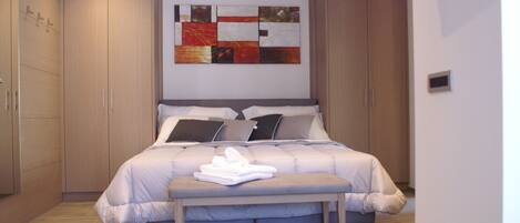 A bedroom with a large bed, a bench, and a wall-mounted artwork.