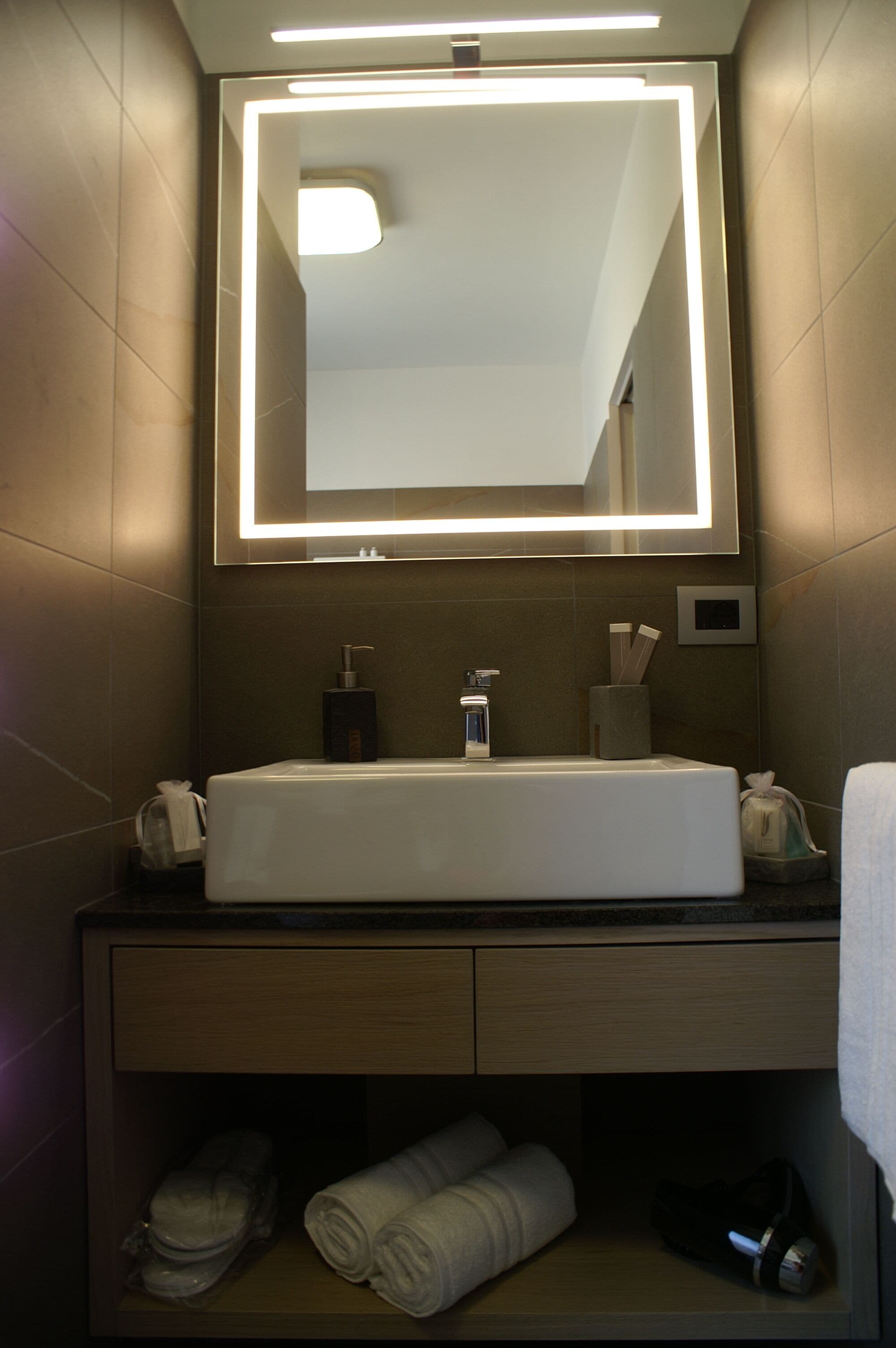 A modern bathroom with a large mirror, a sink, and a towel rack.