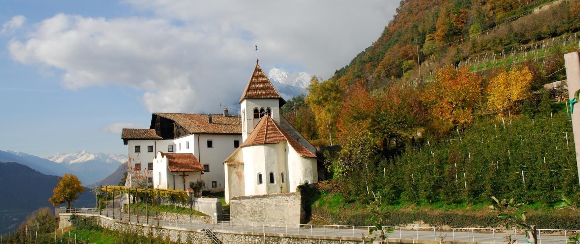 Un edificio tradicional con un campanario, rodeado por una muralla de piedra y un camino pavimentado.