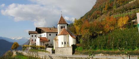 Un edificio tradicional con un campanario, rodeado por una muralla de piedra y un camino pavimentado.