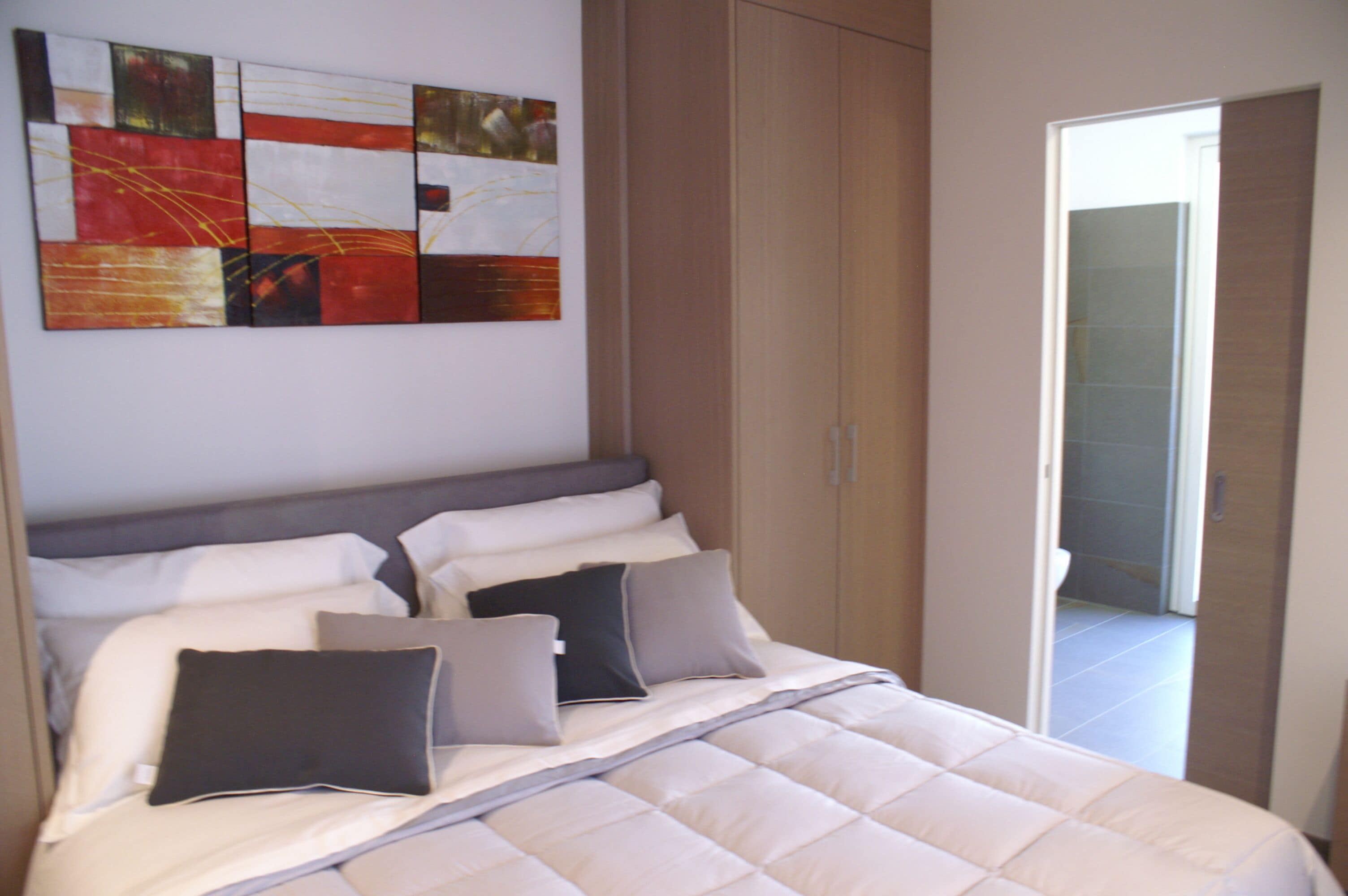 Un dormitorio con cama, almohadas, un armario y un cuadro en la pared.
