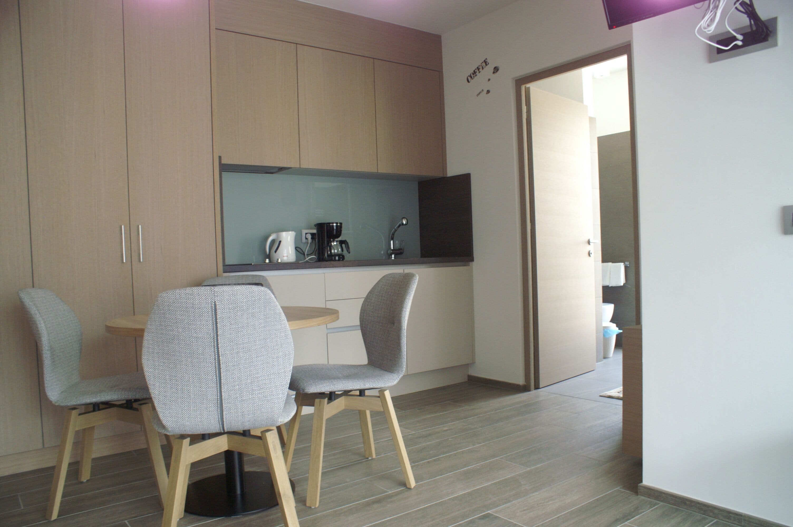 Een moderne keuken met houten kastjes, een ronde tafel en twee grijze stoelen.
