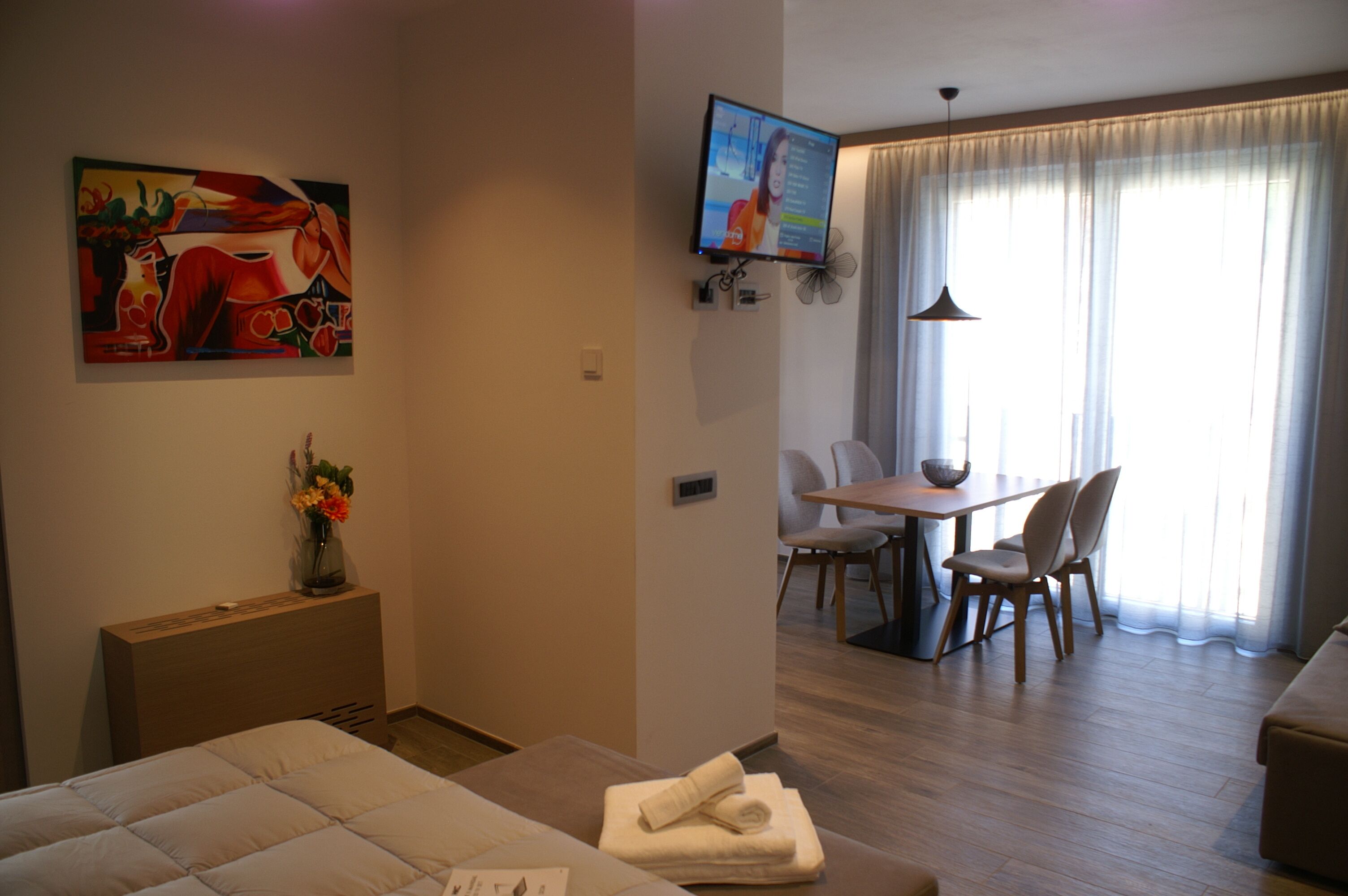 Une chambre d’hôtel comprenant un lit, un bureau, une table à manger avec des chaises, un téléviseur fixé au mur et un tableau accroché au mur.