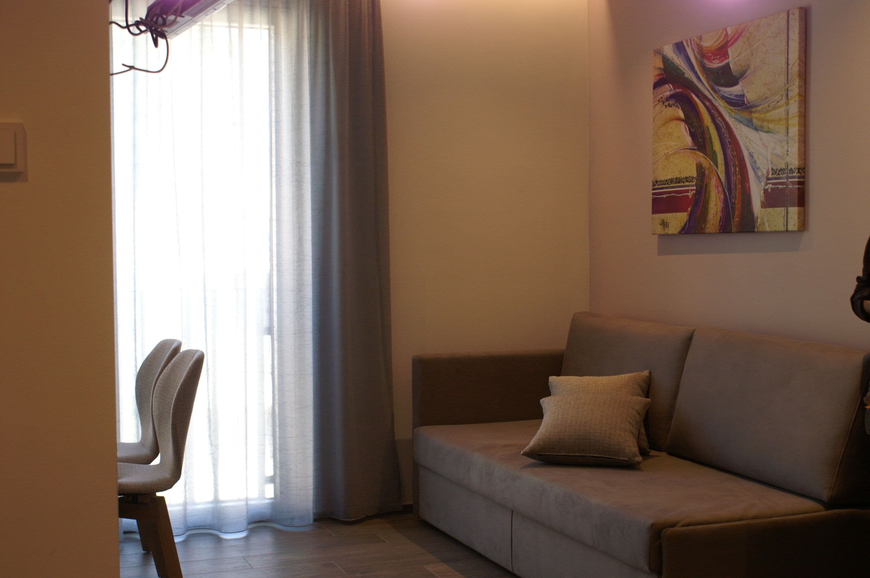 A living room with a sofa, a chair, a painting on the wall, and a window with curtains.