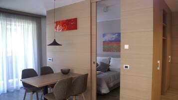 Una habitación moderna con una mesa de madera, sillas, una cama con un cuadro y una puerta corredera.
