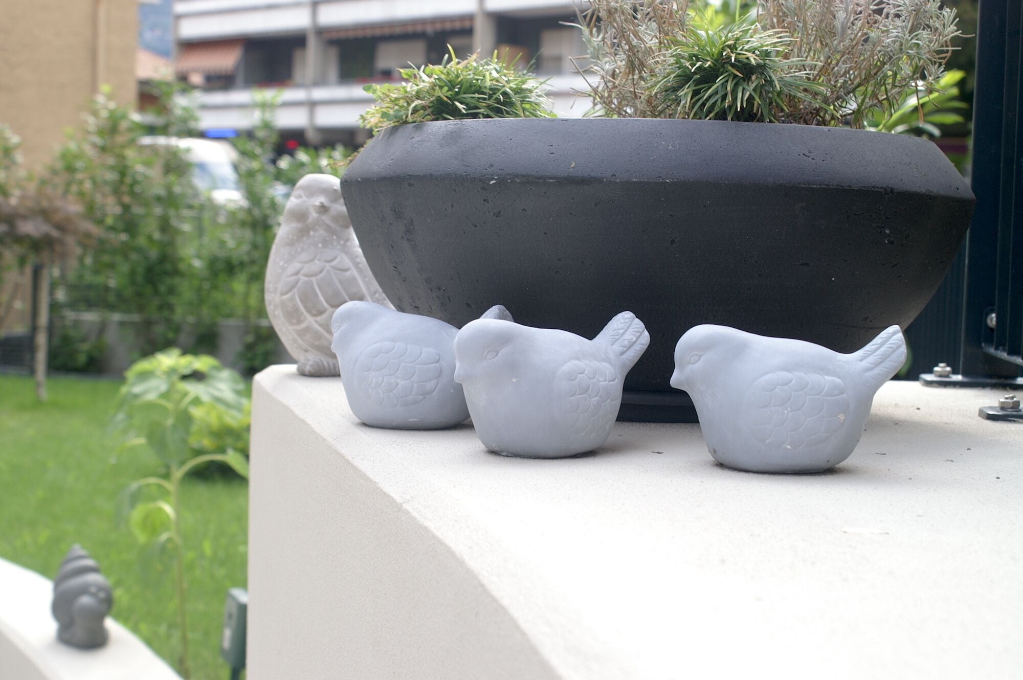 Un vaso nero con tre sculture a forma di uccello bianchi su un balcone.