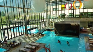 An indoor swimming pool with clear glass walls, lounge areas, and a view of the mountains. - Residence Villa Hedy (Merano)