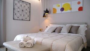 A neatly made bed with a white comforter and pillows, a bedside table with folded towels, and a wall art piece above the bed. - Residence Villa Hedy (Merano)