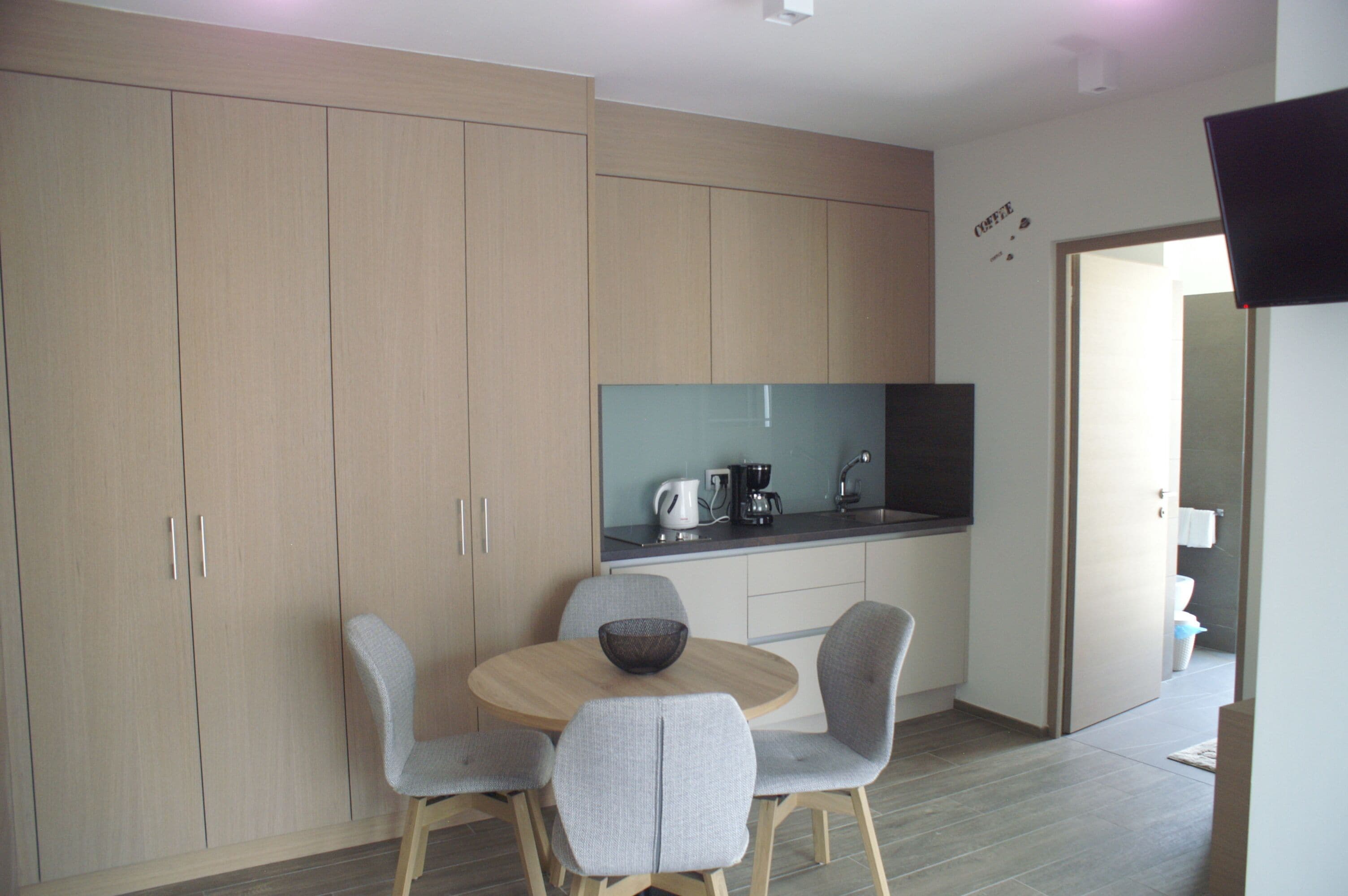 A modern kitchen with a dining area, including cabinets, a coffee maker, and a bowl on the table.