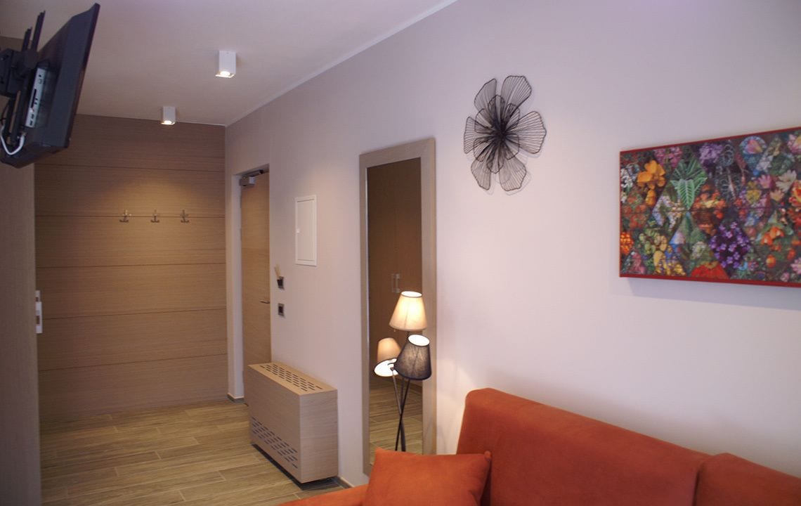 A modern hotel room with a wooden floor, a sofa, a lamp, and a colorful floral painting.