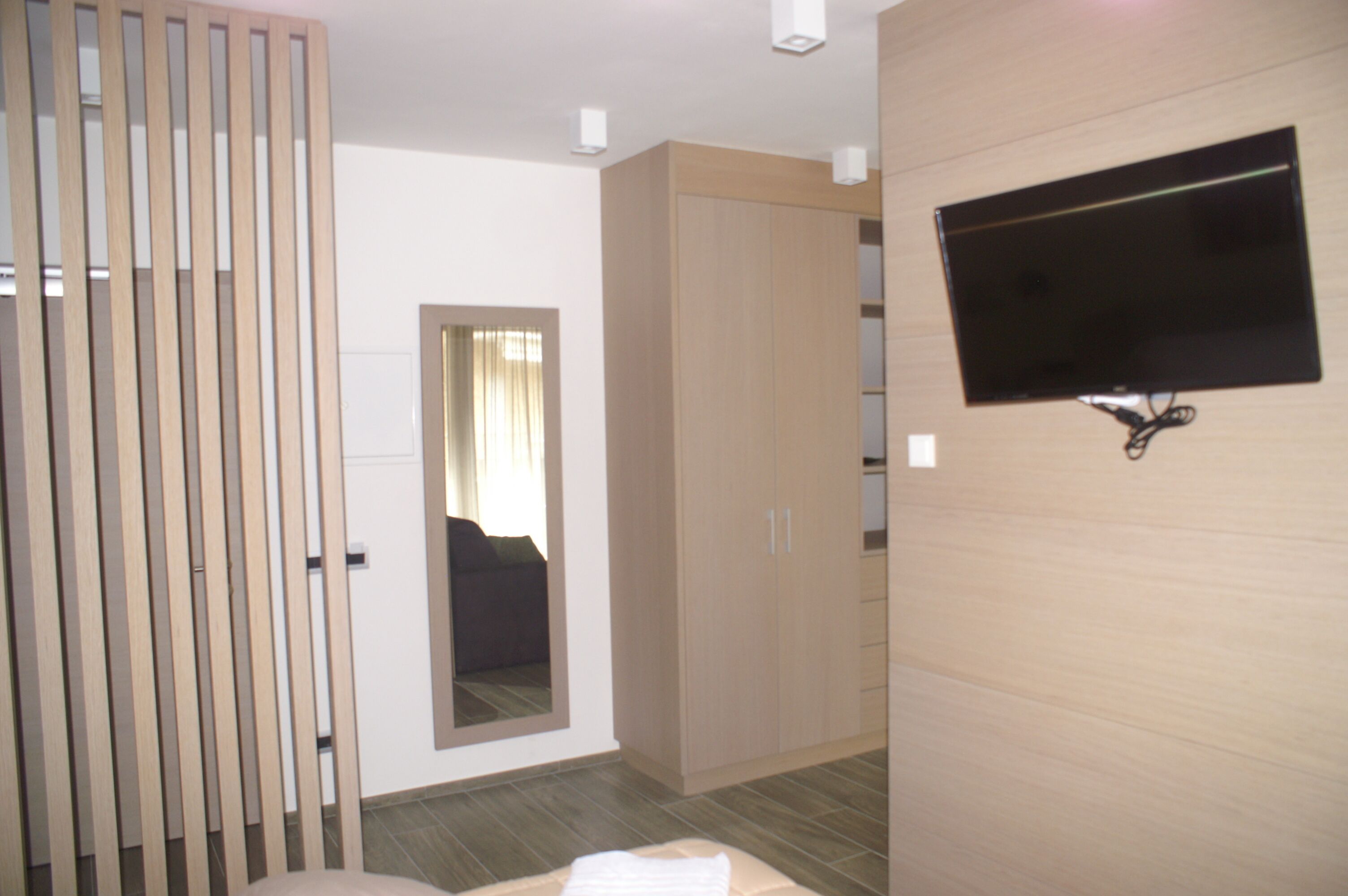 A modern hotel room with a large wardrobe, a flat-screen TV mounted on the wall, and a sliding door.