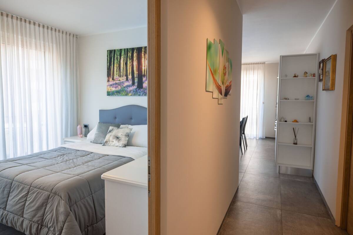 A bedroom with a bed, a nightstand, a painting, and a white shelving unit.