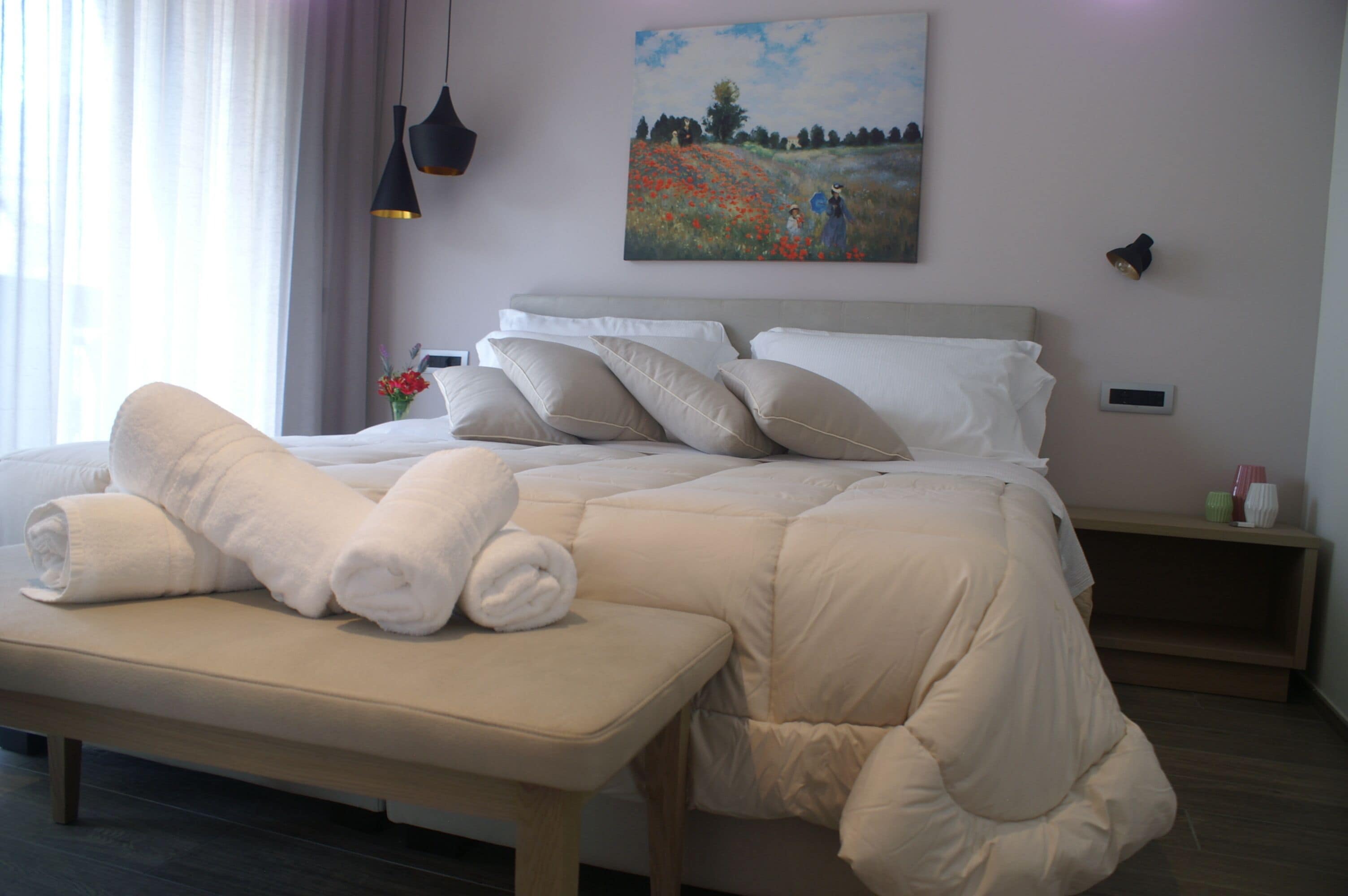 Una cama bien hecha con cubrecolchón acolchado, una mesita de noche con lámpara y un cuadro en la pared.
