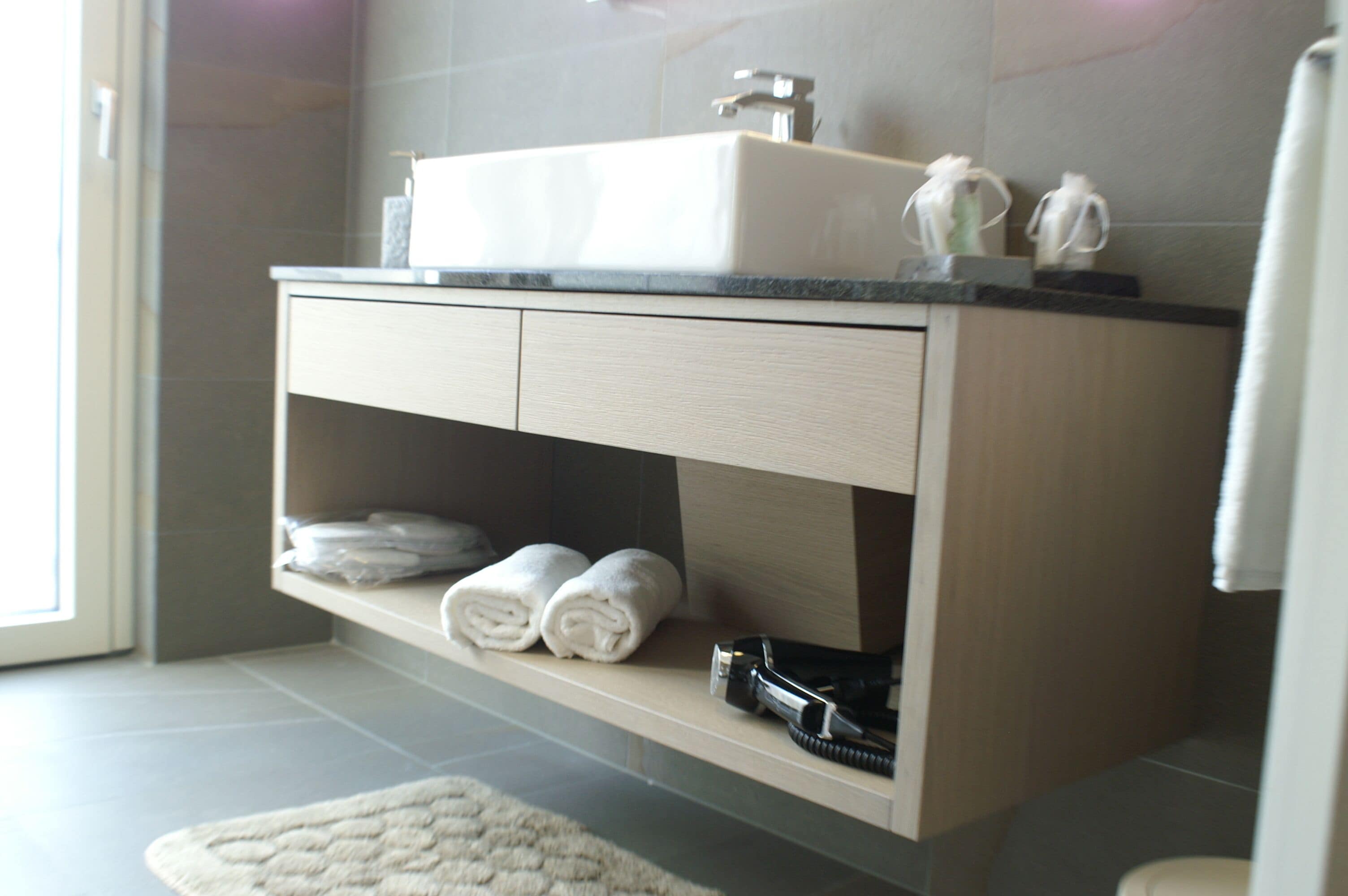 A modern bathroom with a built-in sink, towel rack, and storage shelf.