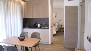 A modern hotel room with a wooden dining table, a kitchen area with a coffee maker, and a bed with a nightstand. - Residence Villa Hedy (Merano)