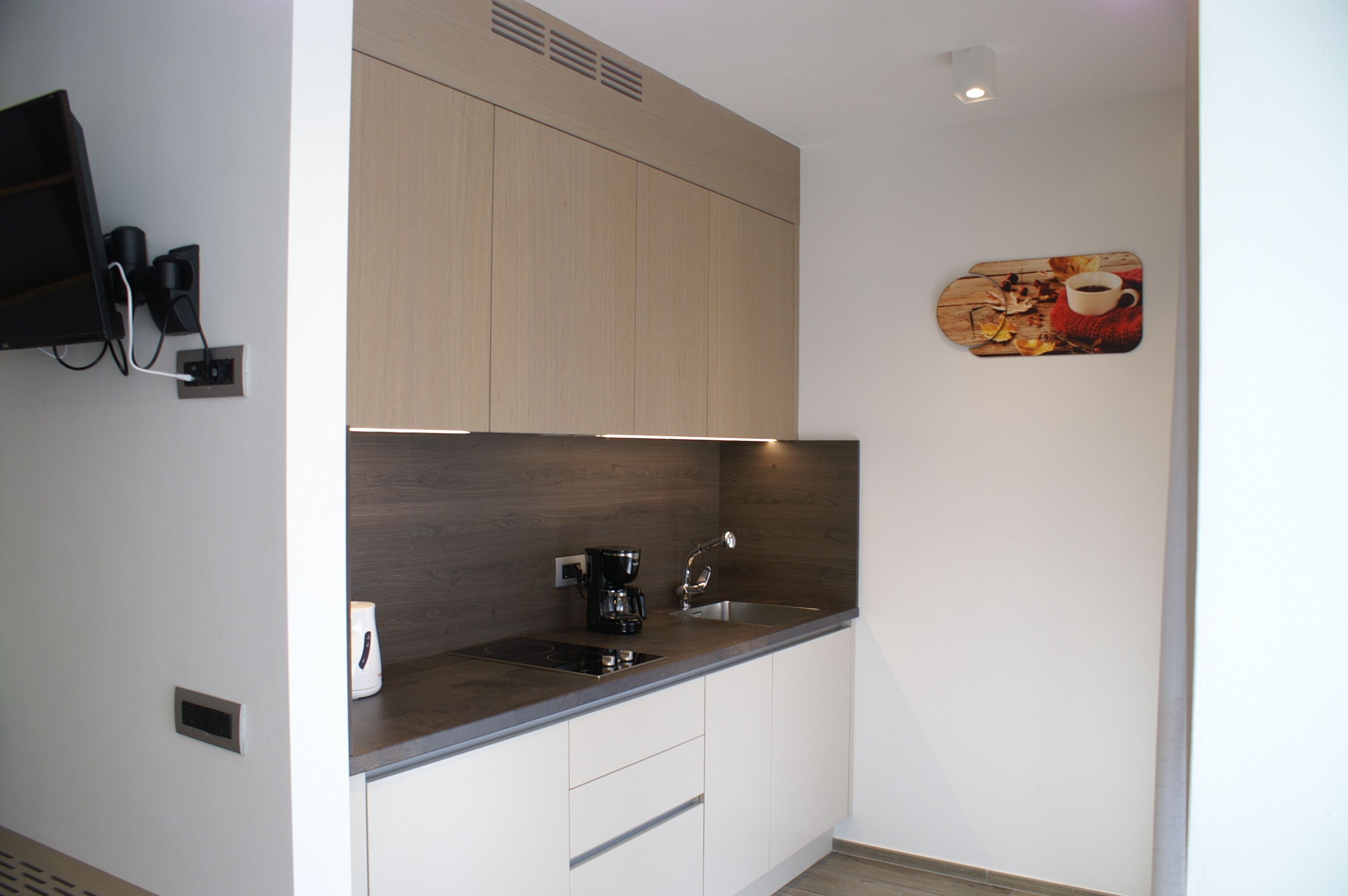 A modern kitchen with a built-in coffee maker, a sink, and a wall-mounted television.