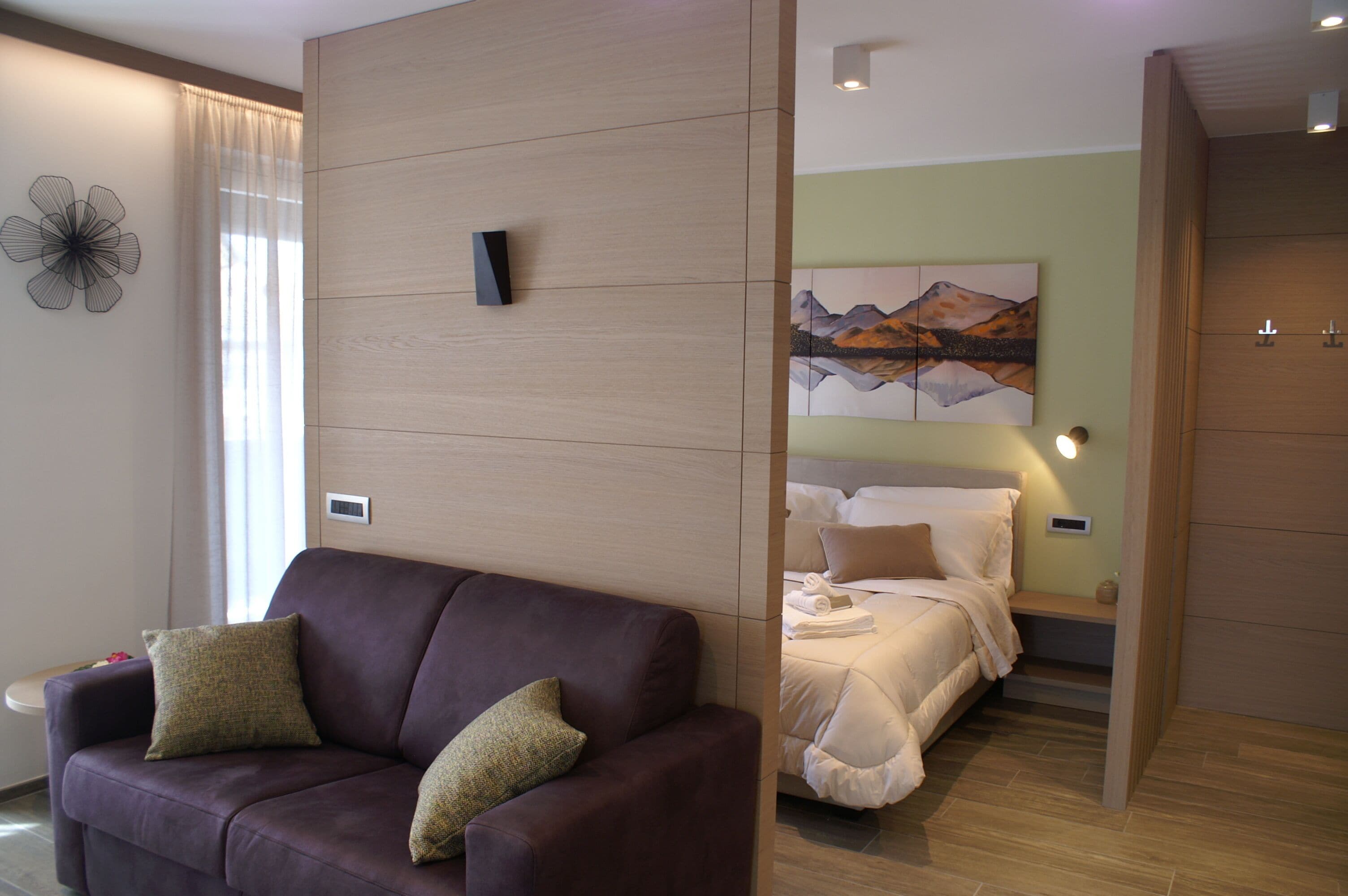 Quarto de hotel moderno com sofá de couro marrom, cama com roupa de cama branca, um quadro na parede e um divisória de madeira.