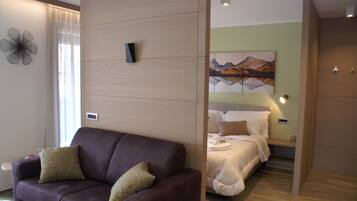 Quarto de hotel moderno com sofá de couro marrom, cama com roupa de cama branca, um quadro na parede e um divisória de madeira.