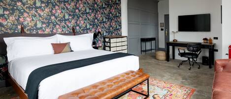 A bedroom with a large bed, a bench, a desk, and a television.