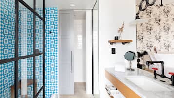 Un baño moderno con un espejo grande, dos lavamanos, una ducha y un revestimiento de baldosas con diseño.