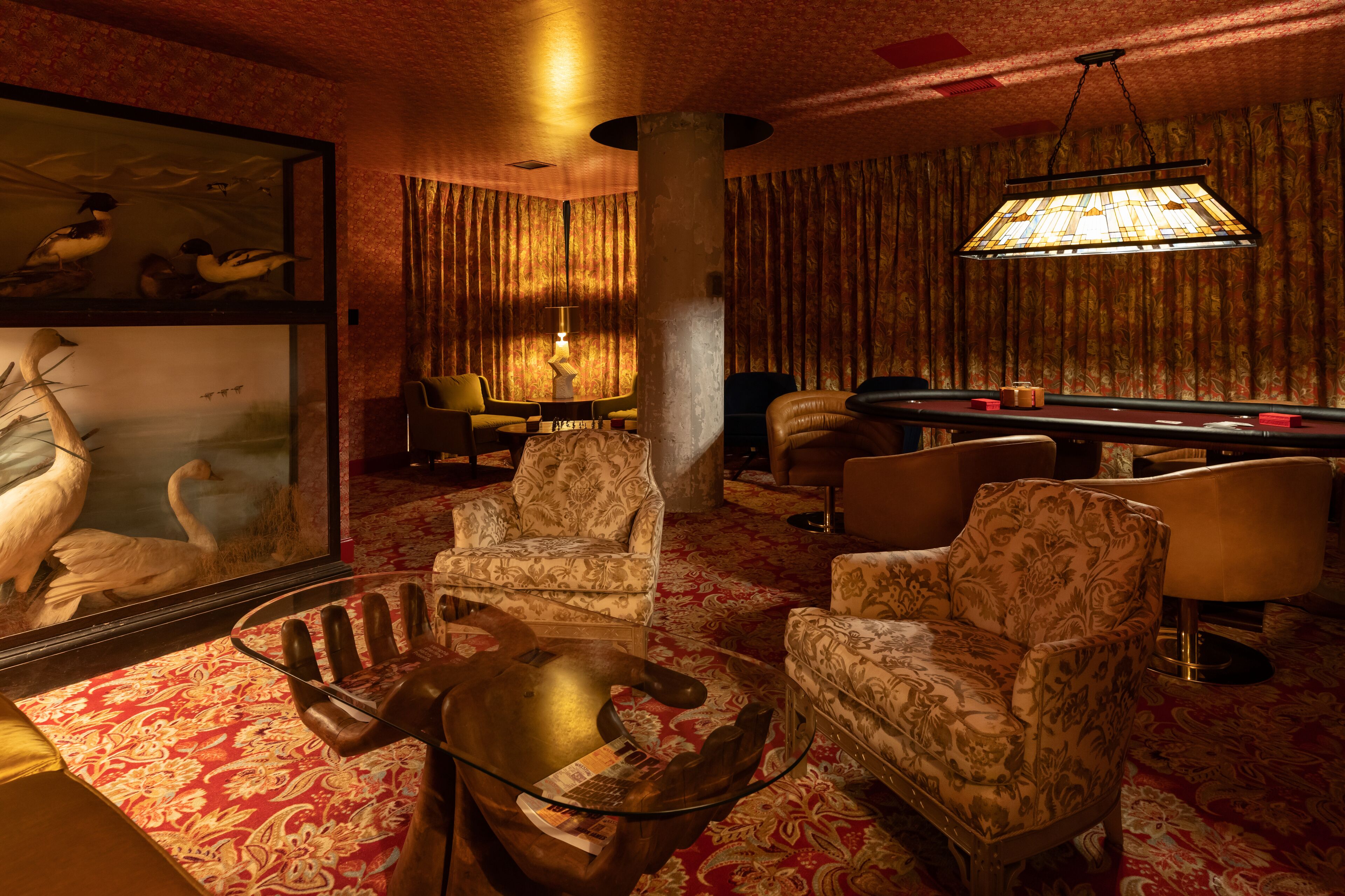 Une pièce comprenant une table de billard, deux fauteuils, une table basse en verre, une lampe et un tableau encadré représentant des oiseaux.