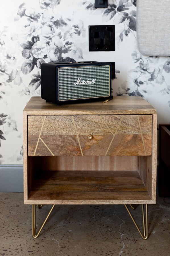 A wooden nightstand with a Marshall speaker on top and a drawer with a brass handle.