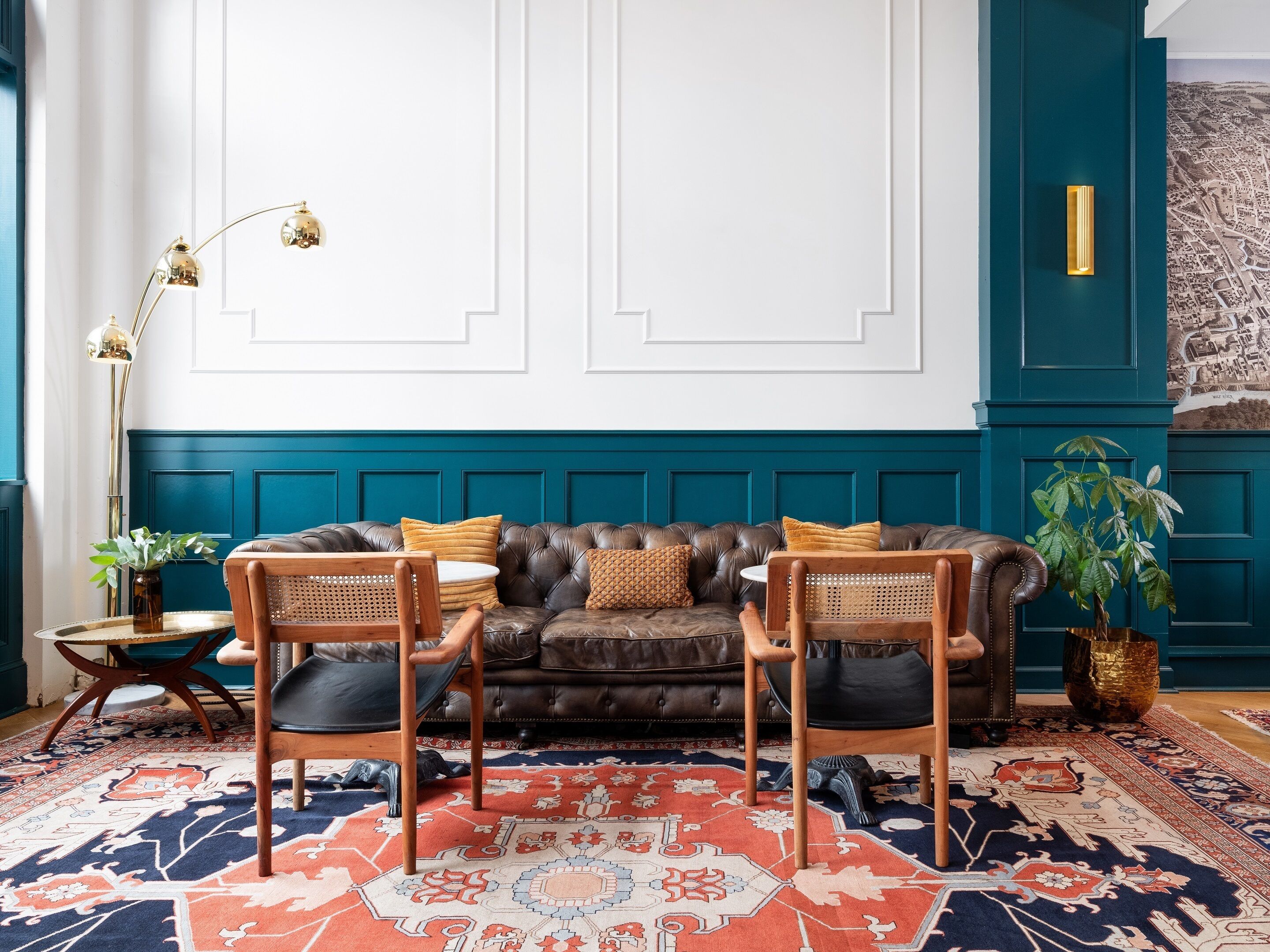 Una sala de estar con una pared de acento color turquesa, un sofá de cuero marrón, dos sillas de madera, un tapete estampado y una lámpara de pie.