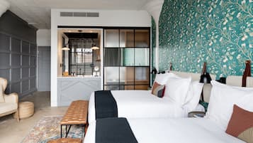 Quarto de hotel com uma cama grande, um banco, um pequeno espaço de estar e vista da cidade pela janela.