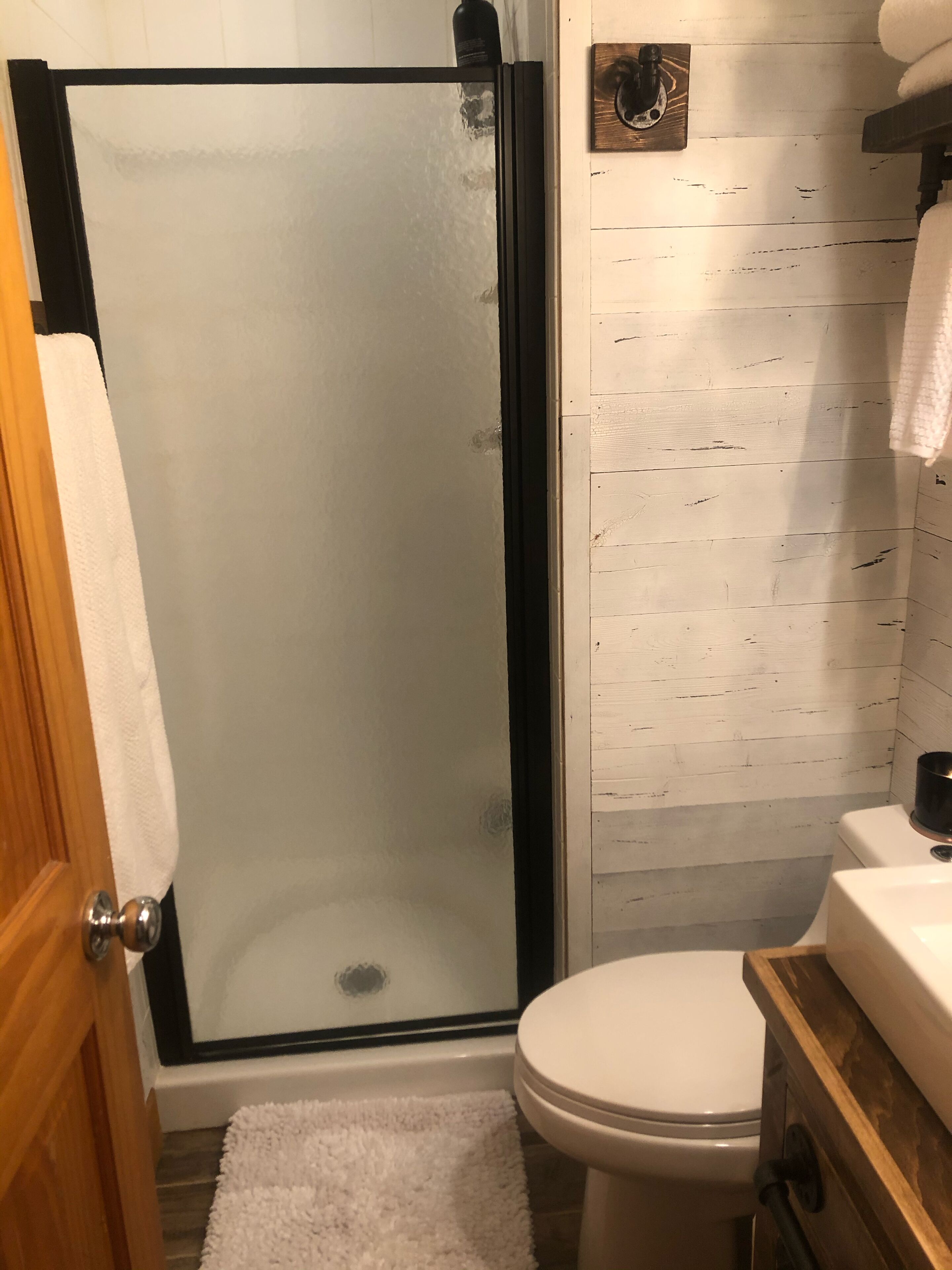 Een badkamer met een douchecabine van glas, een wit toilet en een houten wastafelmeubel.