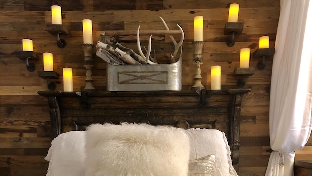 Ein Bett mit weißer Bettwäsche, einem braunen Fellüberwurf und einer weißen Decke mit Pompons.