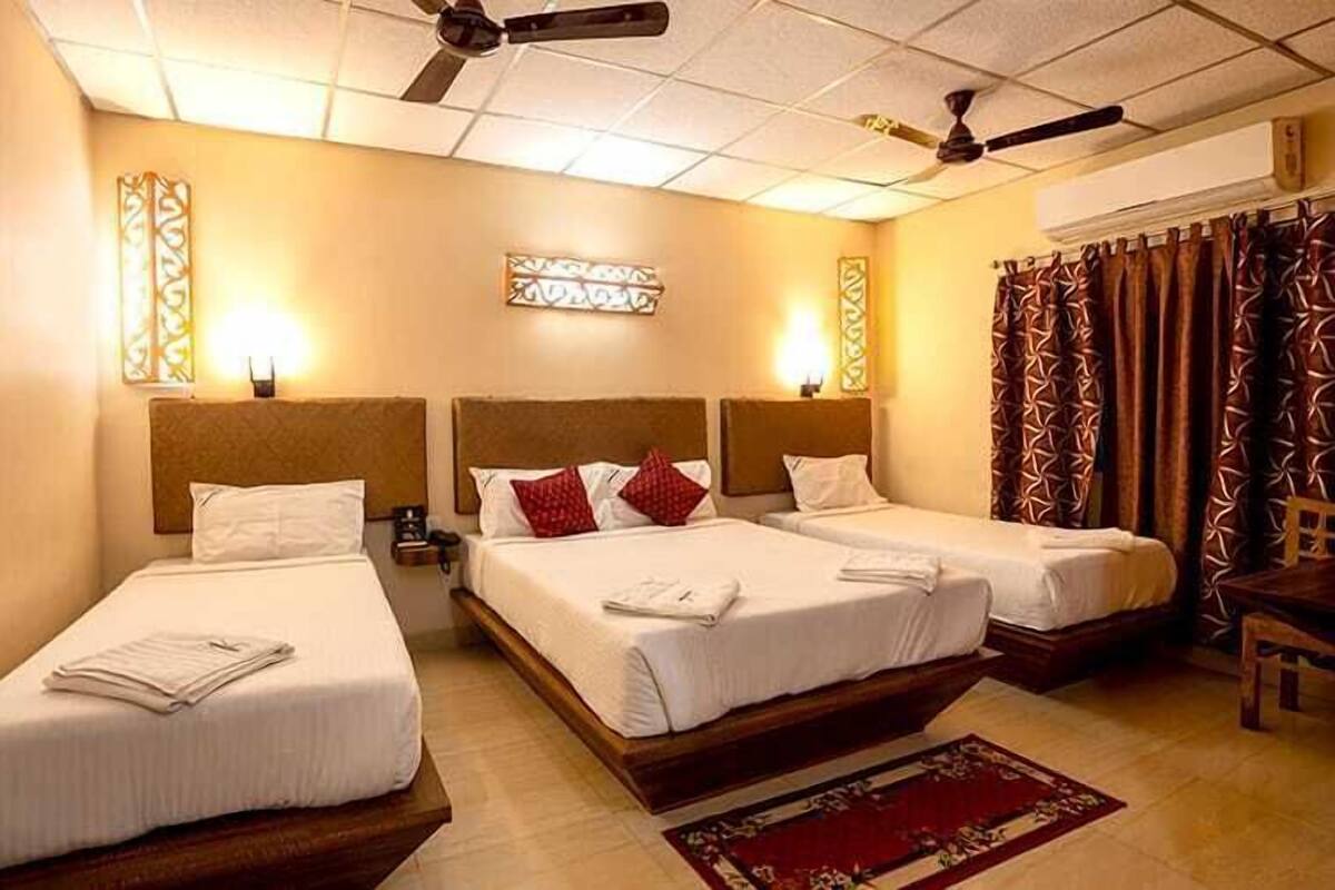 Une chambre d’hôtel avec trois lits simples, un ventilateur de plafond, une table de chevet et un élément décoratif mural.