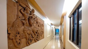 A hallway with a large, detailed wall carving, a long corridor, and a window on the right. - Hotel Shreesh (Port Blair)