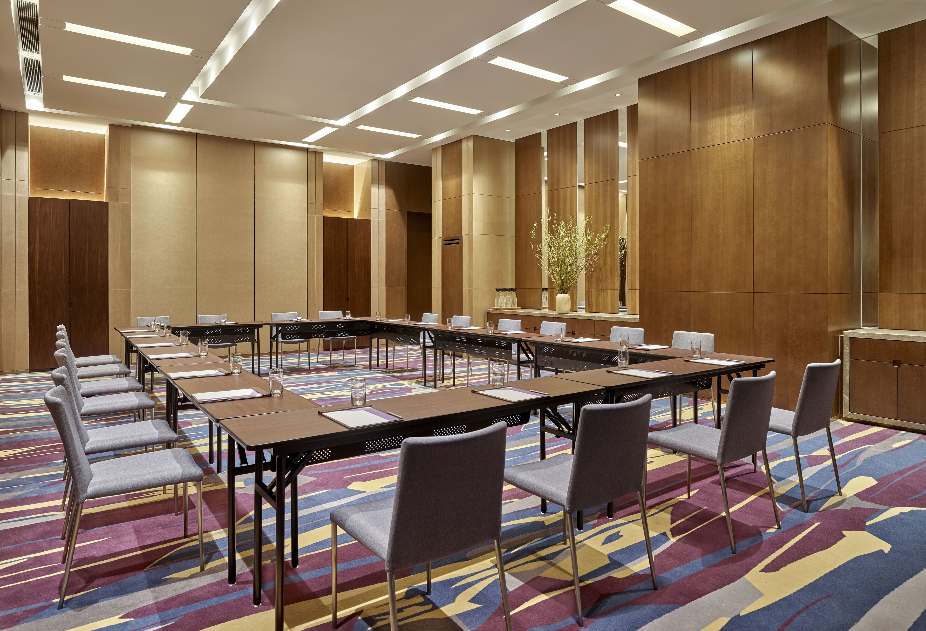 A conference room with a long table, multiple chairs, and a patterned carpet.