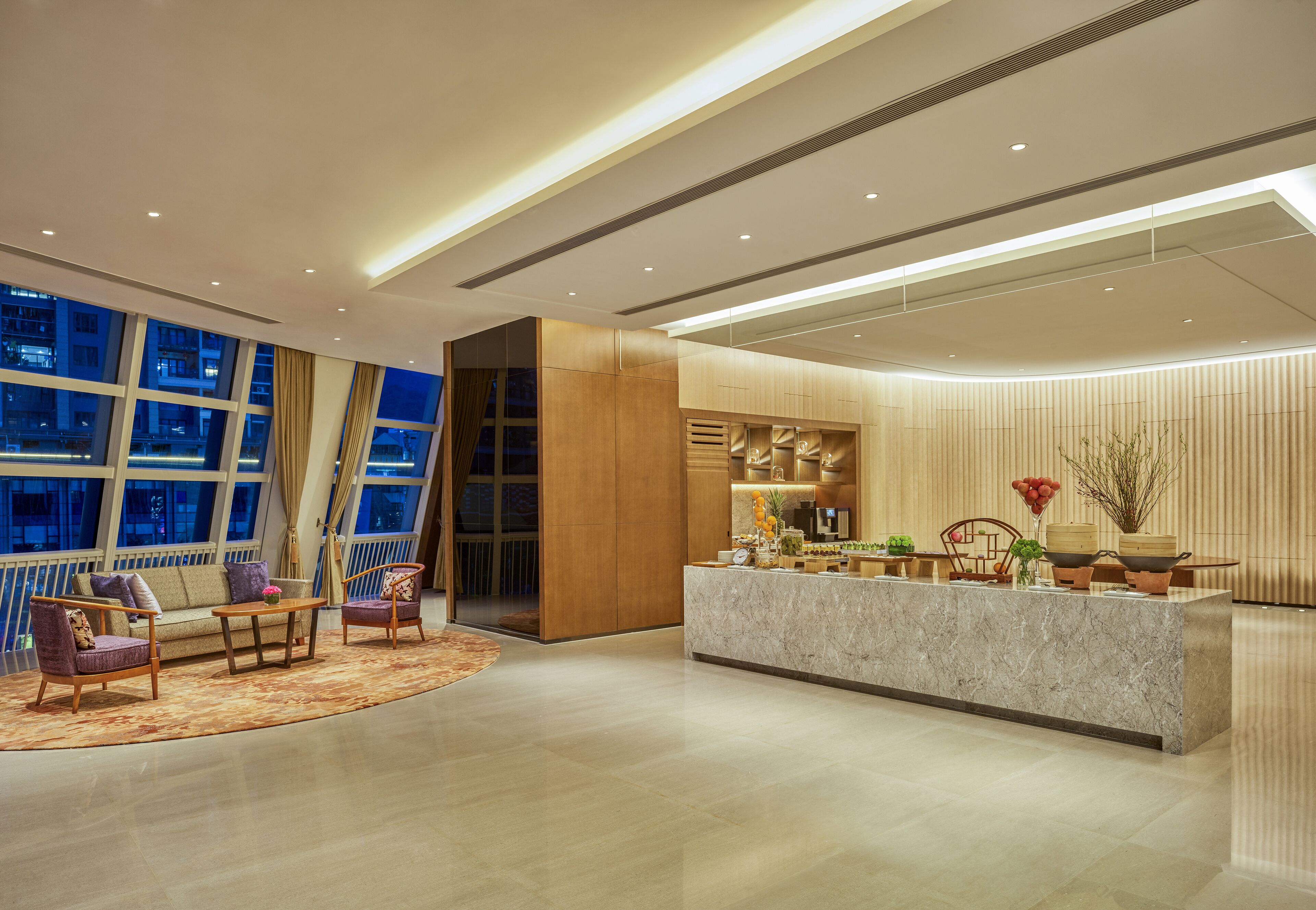 Un vestíbul d'hotel modern amb un taulell de recepció de marbre, zona d'estar confortable, grans finestres i vista a la ciutat.