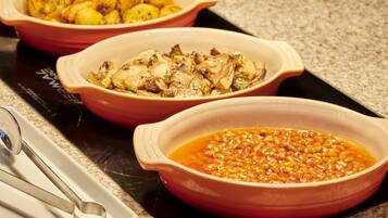 Three ceramic dishes on a stovetop, one with baked potatoes, one with chicken, and one with beans.