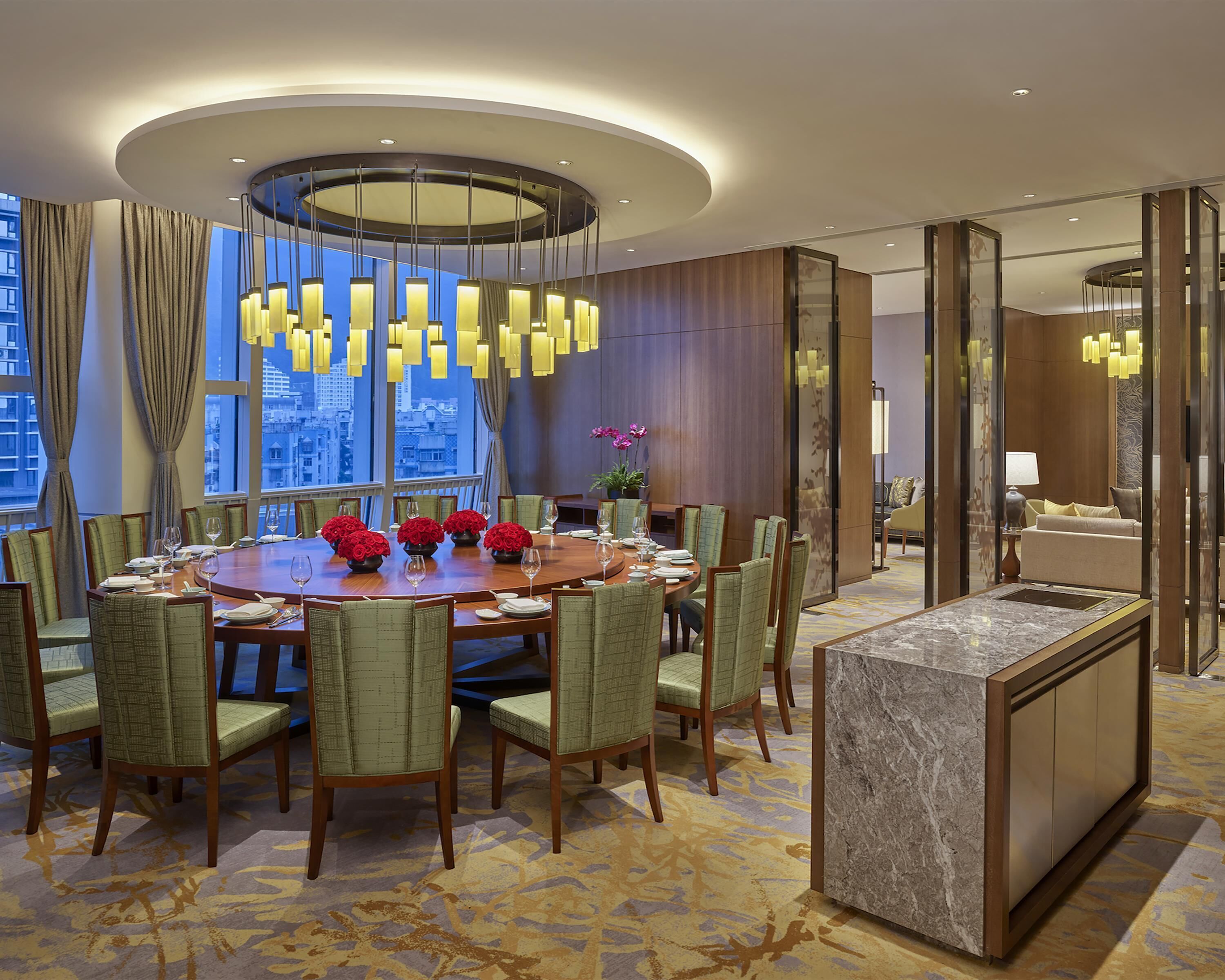 A modern dining area with a round table, green upholstered chairs, and a central chandelier.