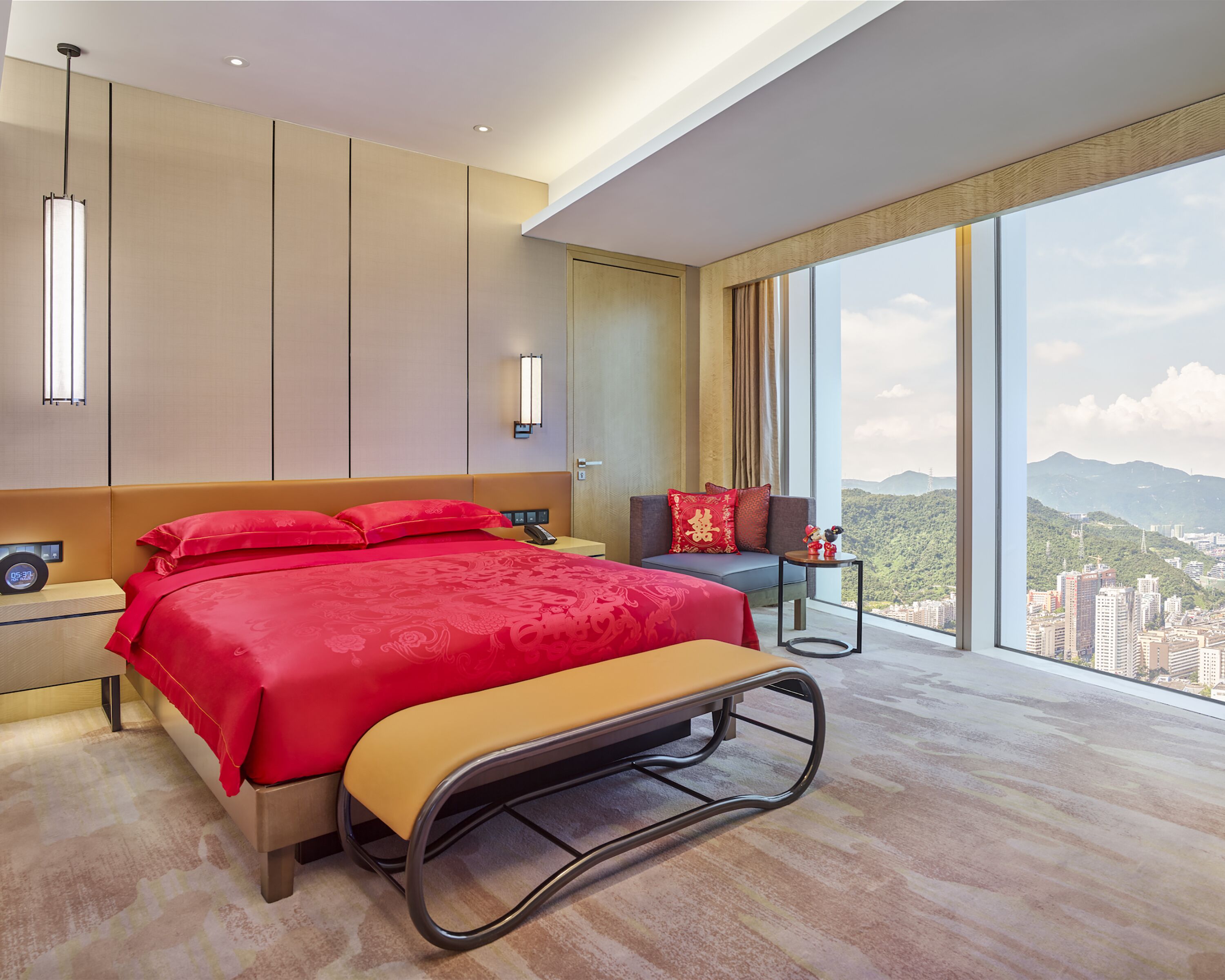 Ein modernes Hotelzimmer mit einem großen Bett, einer Bank, einer Couch und Blick auf eine Stadtlandschaft.
