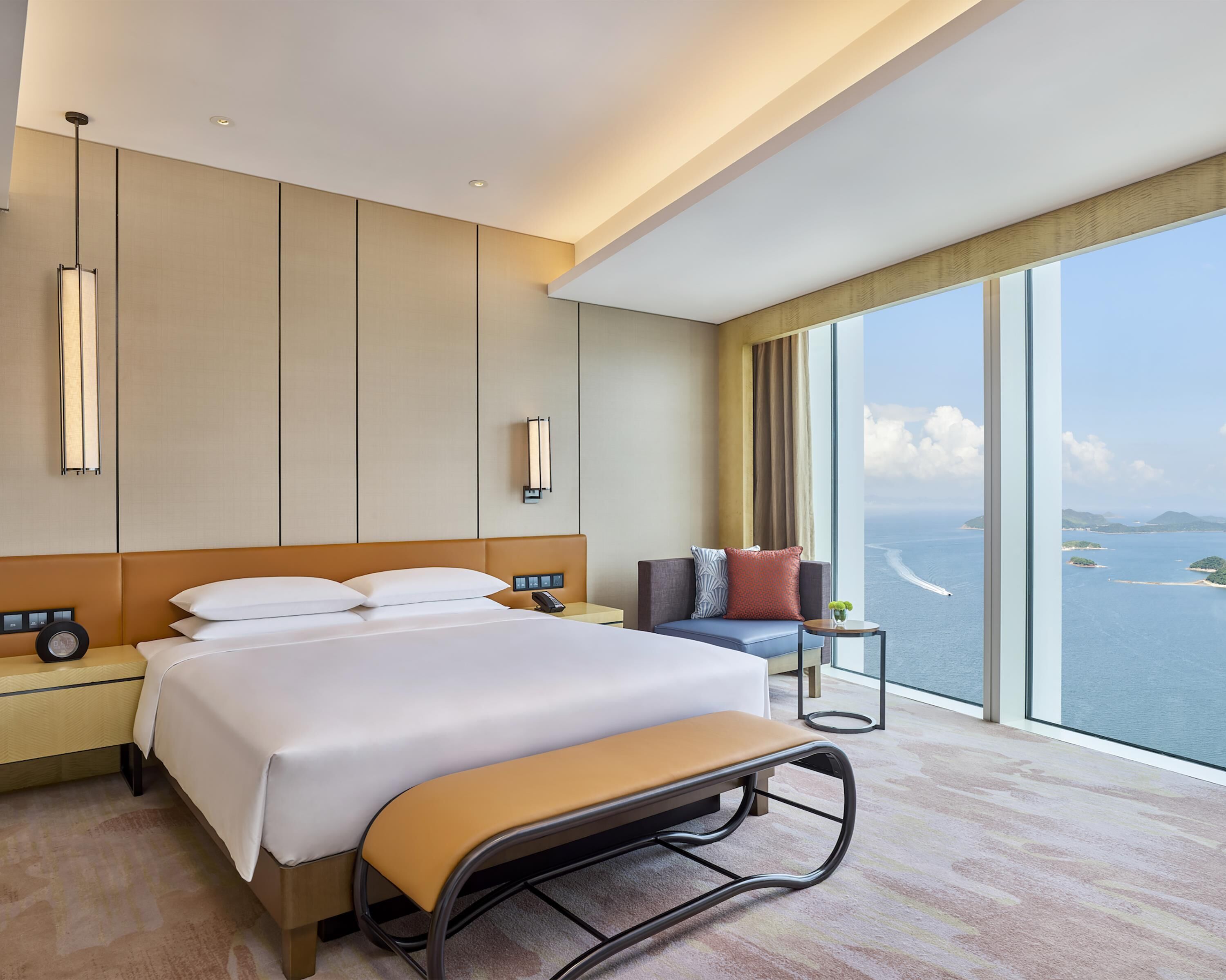 Una camera d'albergo moderna con un letto grande, comodini, una panca, un divano e vista sul mare.