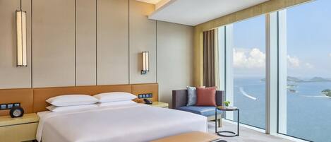 Una camera d'albergo moderna con un letto grande, comodini, una panca, un divano e vista sul mare.