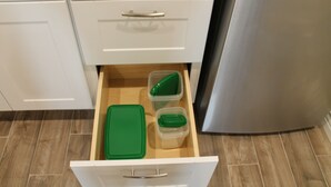 Eine Küchenschublade mit weißem Innenraum, die einen grünen Deckel und zwei klare Plastikbehälter enthält.