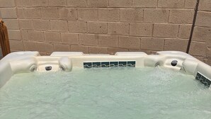 Ein Whirlpool mit Wasser, eine Holzbank und eine Backsteinmauer im Hintergrund.