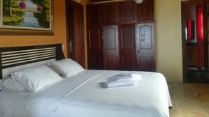 A neatly made bed with white linens in a room with wooden paneling and a painting of a landscape on the wall. - Paratibela Pousada (Anchieta)