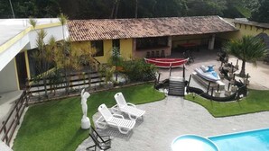 A backyard with a swimming pool, a boat, and lounge chairs. - Paratibela Pousada (Anchieta)