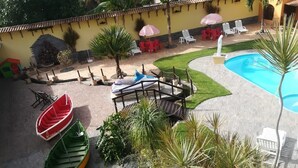 A pool area with lounge chairs, a small pool, and two boats. - Paratibela Pousada (Anchieta)